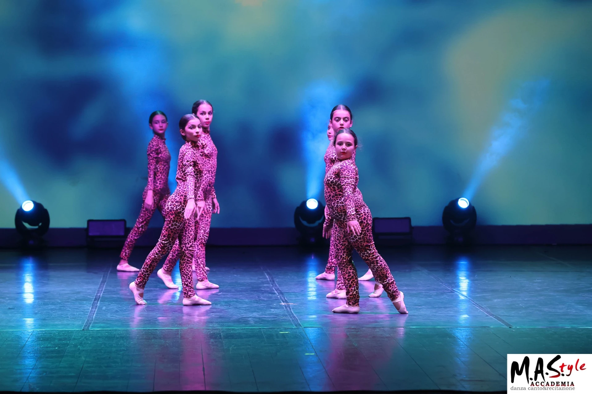 Giovani allieve di M.A.Style in tutine leopardate rosa danzano su un palco con fari blu e scarpette da danza