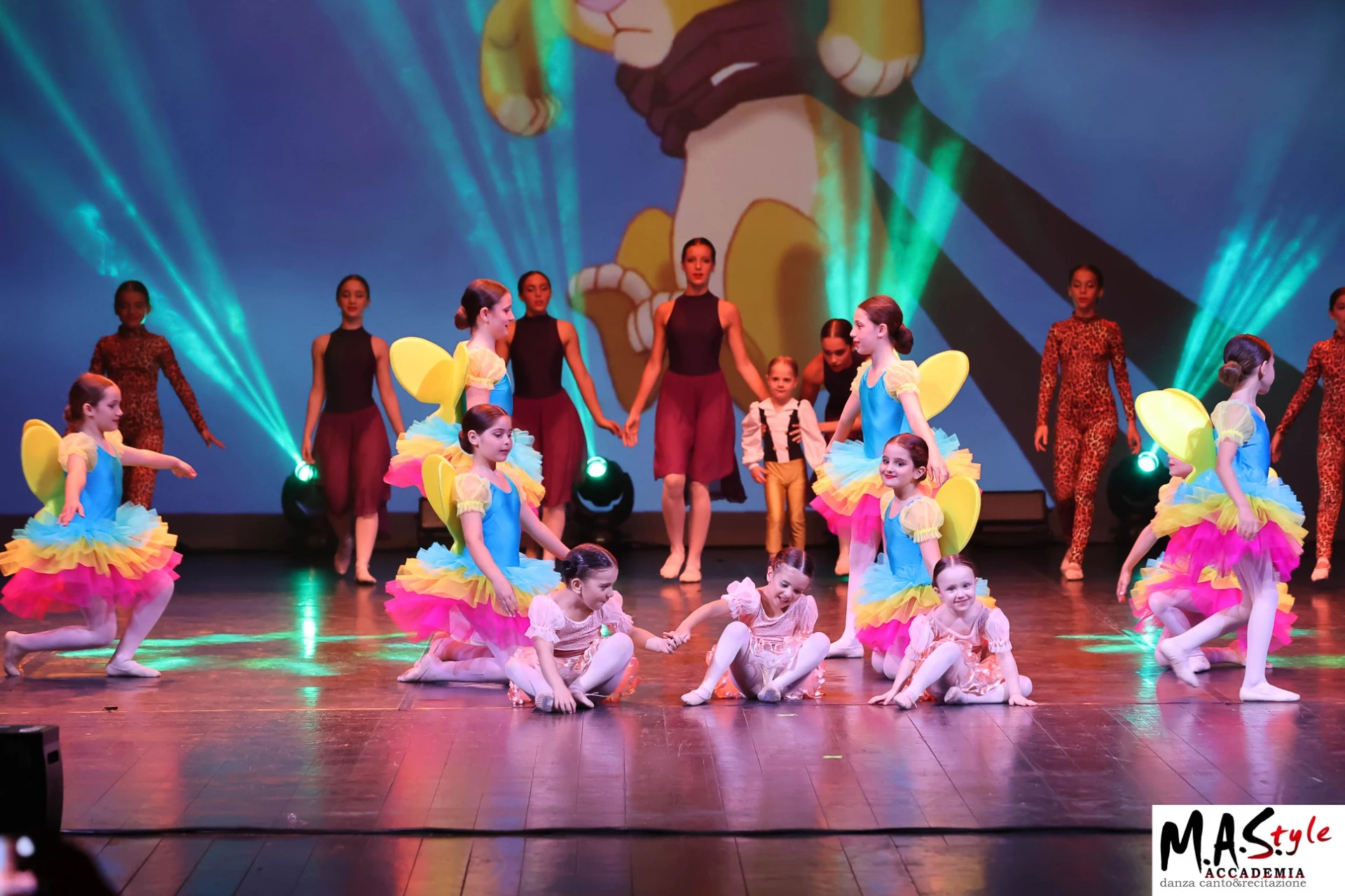 Allieve di M.A.Style in tutù arcobaleno con ali gialle danzano sul palco tra luci verdi e ragazze in body bordeaux